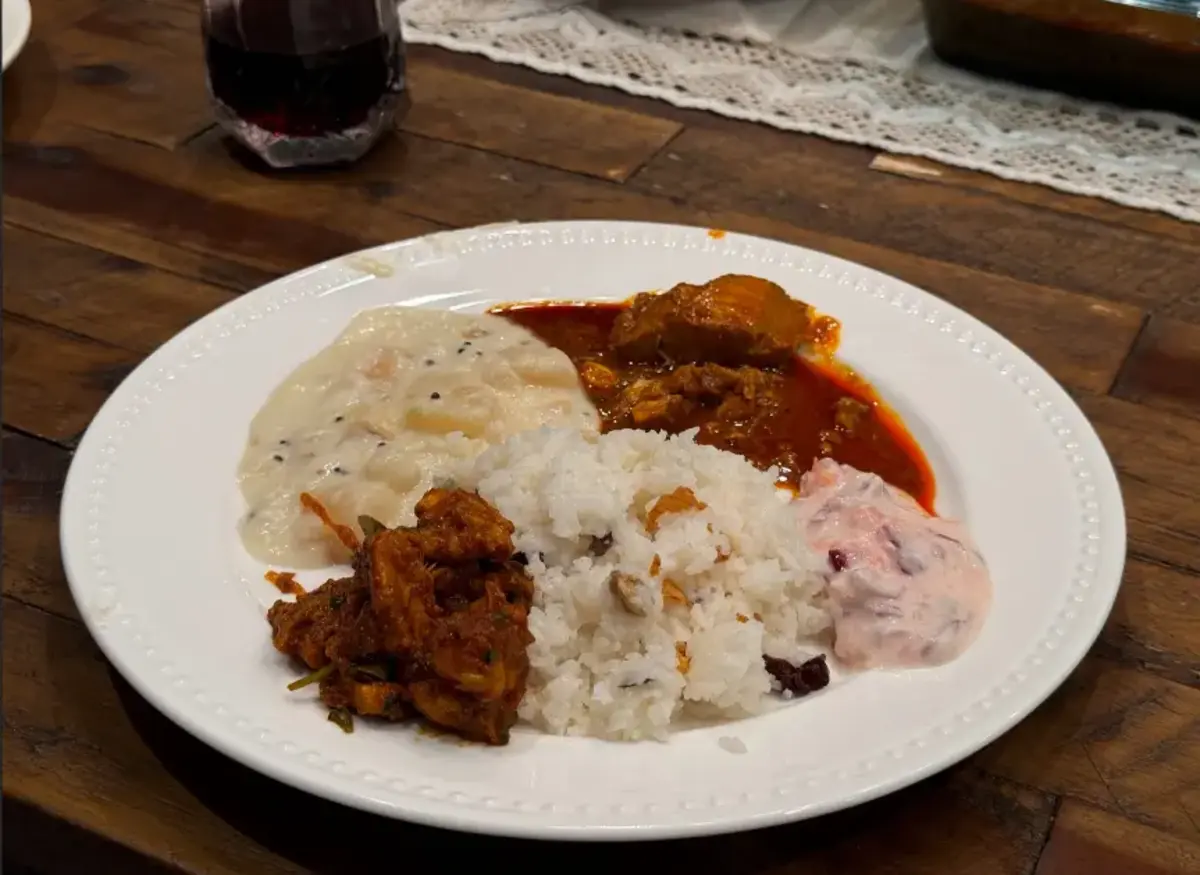 Chicken Ghee Roast served with Ghee Rice, Nadan Chicken Curry, and Onion Raita on a white plate.
